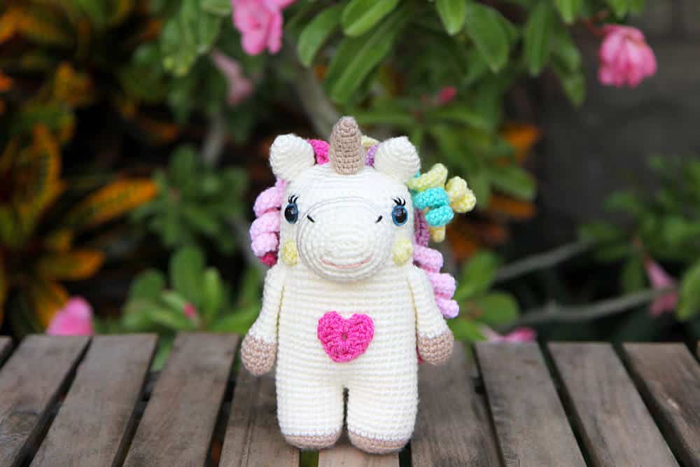 crochet unicorn amigurumi with a colourful mane and a heart on its belly