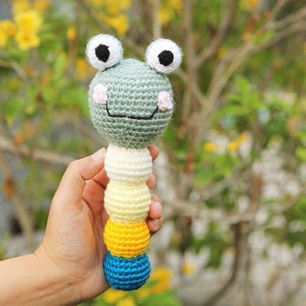 An amigurumi frog baby rattle in a hand