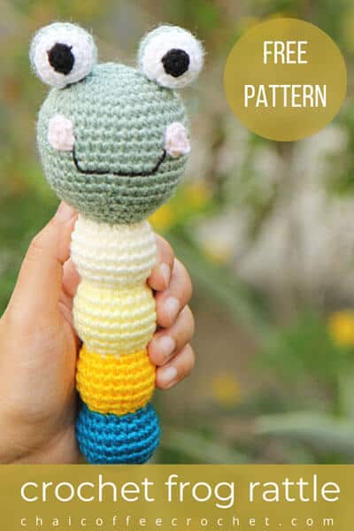 a crocheted frog baby rattle in a hand. The text says " crochet frog rattle free pattern"