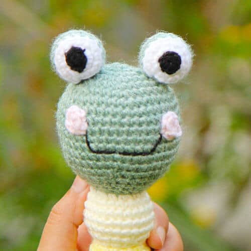 A close up of the head of a crocheted frog rattle