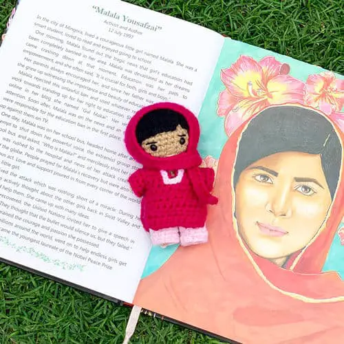 Amigurumi crochet Malala doll on a book with Malala's photograph and the text saying "Malala Yousafzai" with a story about her