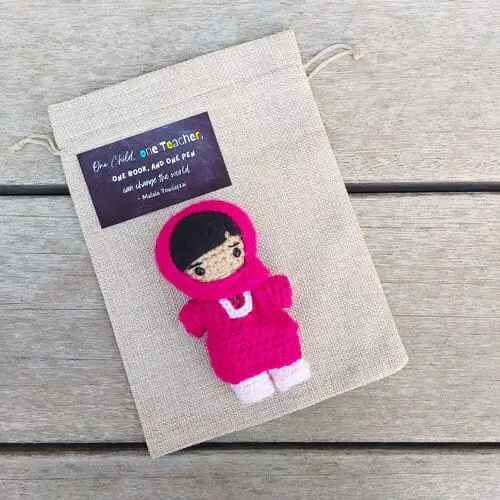 Crochet Malala Yousafzai doll with a tag saying "One child, one teacher, one book, and one pen can change the world"