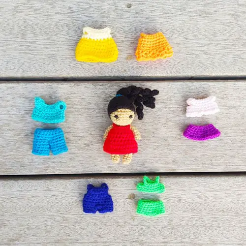 small crochet dress up doll in the center with removable clothes from her wardrobe around her