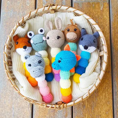 crochet baby rattles of a fox, frog, bunny, monkey, wolf, hippo, and dinosaur in a basket 