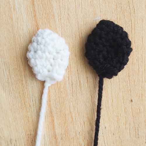 two crochet cow ears. one is black and the other white.