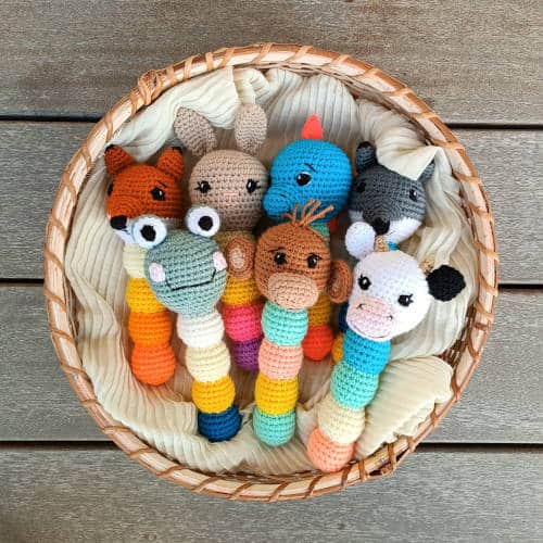 7 animal crochet baby rattles in a basket: a cow, monkey, frog, wolf, dinosaur, bunny, and fox