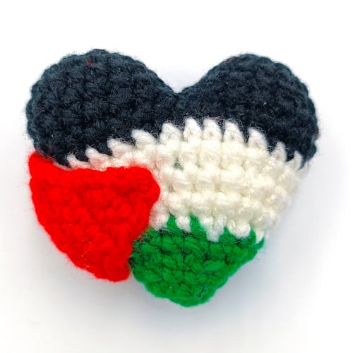 crochet Palestine flag heart. The heart is in black on top, followed by white, followed by green. There is a red triangle on the side.
