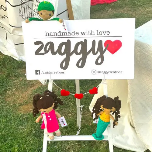 Craft show sign with dolls sitting on the sign