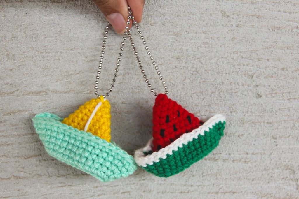 two crochet boat keychain. One is yellow and green and the other is designed like a watermelon